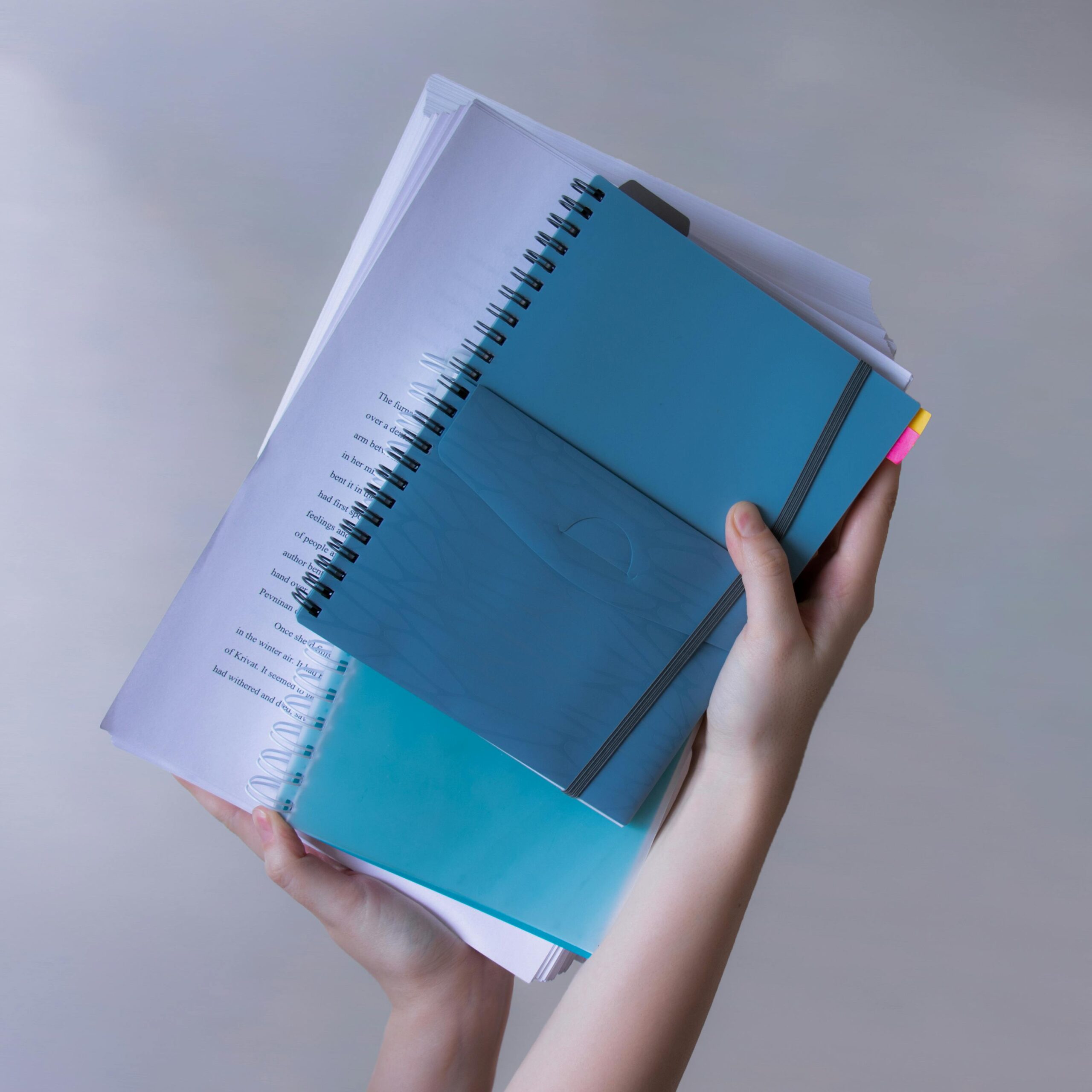 Hands hold blue spiral-bound notebooks and papers, showcasing organization and study.