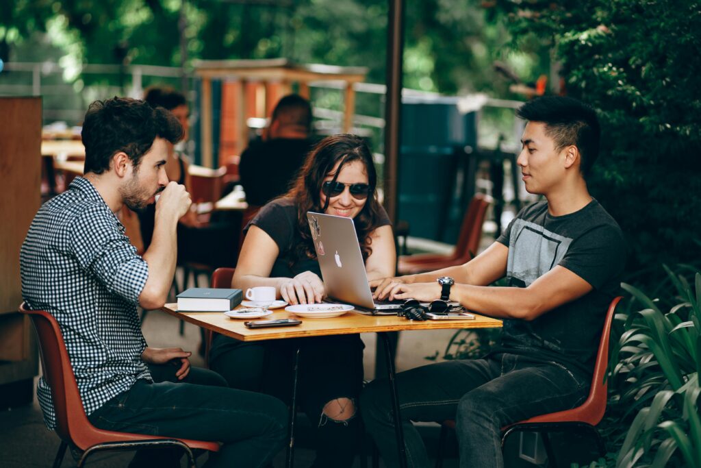 pexels-photo-933964-933964 A group of young adults working on a laptop at an outdoor coffee shop, enjoying teamwork and collaboration.